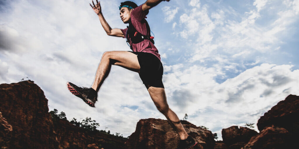 side view of trail runner jumping on the horizon and stone